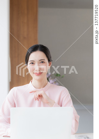 デスクで座るパソコンの仕事をするピンクの服を着た綺麗な女性 カメラ目線 デスクで座るパソコンの仕事をするピンクの服を着た綺麗な女性 カメラ目線 137719520