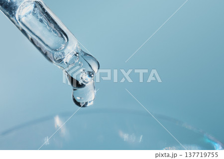 Droplets of cosmetic fluid dropping from pipette against blue background 137719755