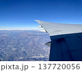 飛行機の窓から見た、青空と雪山の上を飛ぶ航空機の翼の風景 137720056