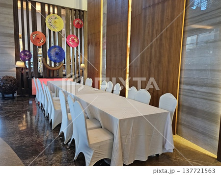 An elegant banquet setup featuring a long dining table with white tablecloths and chair covers, set against a modern interior wall decorated with vibrant An elegant banquet setup featuring a long dining table with white tablecloths and chair covers, set against a modern interior wall decorated with vibrant 137721563