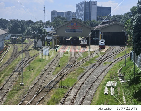 A wide-angle, high-angle shot captures the bustling activity at the Bandung Locomotive Depot in Indonesia, featuring several KAI trains parked on multiple tracks under a clear, bright blue sky. A wide-angle, high-angle shot captures the bustling activity at the Bandung Locomotive Depot in Indonesia, featuring several KAI trains parked on multiple tracks under a clear, bright blue sky. 137721948