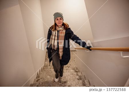 Woman walking down stairs wearing a scarf and a beanie during the winter season Woman walking down stairs wearing a scarf and a beanie during the winter season 137722588