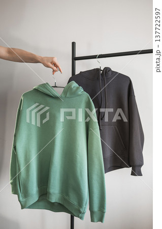 Hand holding two hoodies on display in a clothing shop during the day 137722597