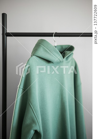 Green hoodie hanging on a black rack in a simple room with plain walls 137722609