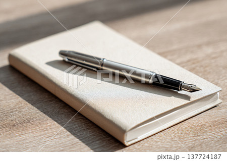 手帳の上に置かれた万年筆と木製デスクのワークスペースイメージ 137724187