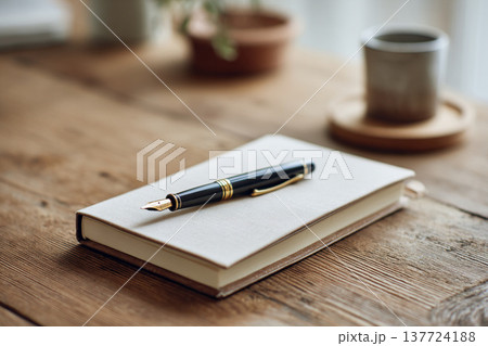 手帳の上に置かれた万年筆と木製デスクのワークスペースイメージ 137724188