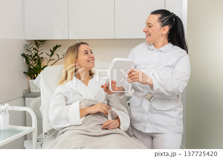 Middle-aged woman smiling in mirror after cosmetic procedure in clinic with visible skin results Middle-aged woman smiling in mirror after cosmetic procedure in clinic with visible skin results 137725420