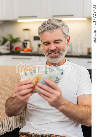 Middle-aged man counts money cash euros smiles at big plans purchase salary bonus savings investment Middle-aged man counts money cash euros smiles at big plans purchase salary bonus savings investment 137725433