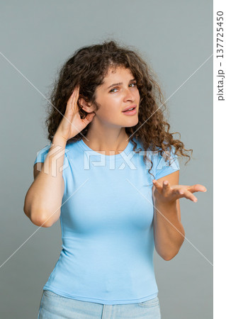 Woman holding hand near ear gesture listening carefully indicating cannot hear confused reaction 137725450