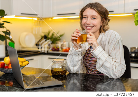 Young woman happily drinking fresh hot tea in cozy kitchen during diet break and home leisure time 137725457