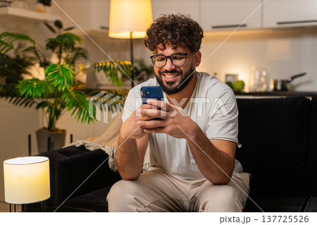 Arabian man gets happy message from friend on smartphone replies with smile texting at night indoors 137725526