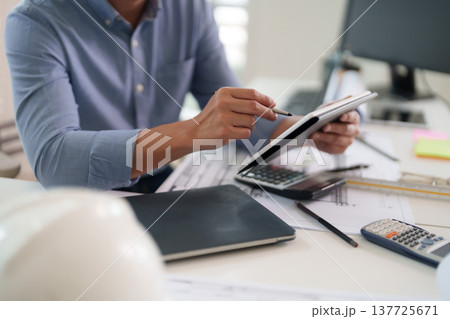 Asian adult man engineer architect using digital tablet stylus at modern office workspace reviewing blueprints project plans calculating data Asian adult man engineer architect using digital tablet stylus at modern office workspace reviewing blueprints project plans calculating data 137725671