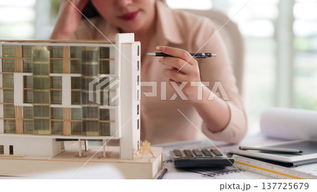 Asian adult woman architect designs building model plans construction project at modern office studio workspace demonstrating precise urban development strategy Asian adult woman architect designs building model plans construction project at modern office studio workspace demonstrating precise urban development strategy 137725679