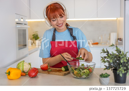 Young woman slices cucumber tomato on cutting board makes colorful salad and tastes fresh bite smile Young woman slices cucumber tomato on cutting board makes colorful salad and tastes fresh bite smile 137725729
