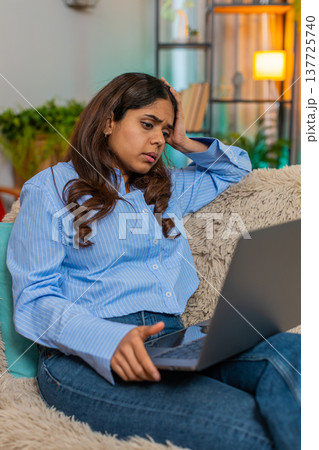 Indian woman holding head in fatigue while looking at laptop screen, tired and exhausted expression Indian woman holding head in fatigue while looking at laptop screen, tired and exhausted expression 137725740