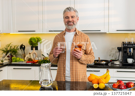 Middle-aged man checks smartphone while drinking water in kitchen for healthy diet hydration routine Middle-aged man checks smartphone while drinking water in kitchen for healthy diet hydration routine 137725847