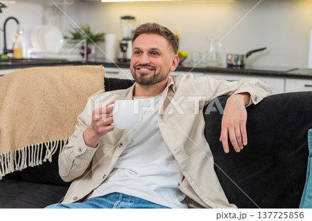 Young man enjoys herbal tea holds warm cup smiles breathes aroma takes pause and feels gentle relief Young man enjoys herbal tea holds warm cup smiles breathes aroma takes pause and feels gentle relief 137725856