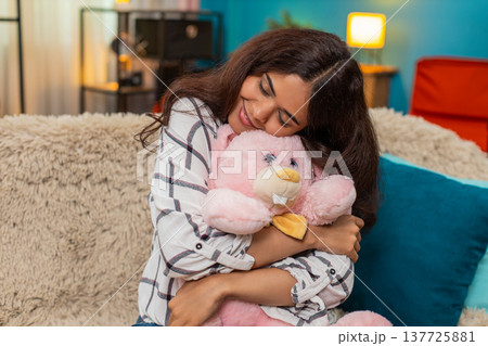 Indian woman holding pink bunny toy smiling nostalgic memory emotion missing childhood child indoors Indian woman holding pink bunny toy smiling nostalgic memory emotion missing childhood child indoors 137725881