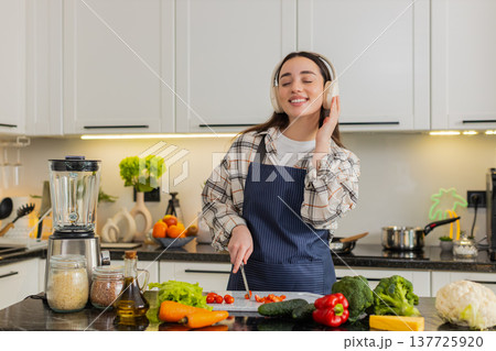 Young woman cutting cherry tomatoes listening to music preparing fresh vegetarian salad at home meal 137725920