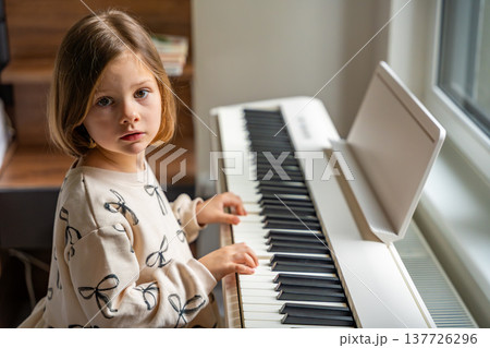 Home lesson on music for the girl on white piano synthesizer. Concept of early development: learning music enhances motor skills, hearing, and intelligence, fostering creativity from childhood Home lesson on music for the girl on white piano synthesizer. Concept of early development: learning music enhances motor skills, hearing, and intelligence, fostering creativity from childhood 137726296