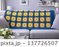 A knitted throw with a floral pattern on a sofa in a bright living room. AI 137726507