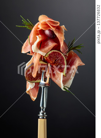 Prosciutto with figs, rosemary, and red olives on a fork. 137726832