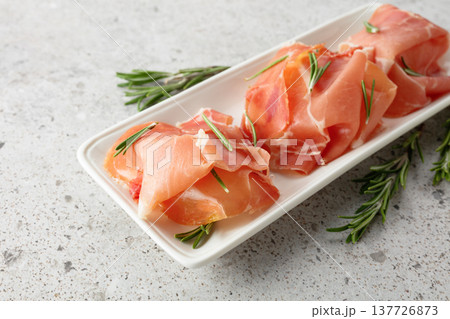 Prosciutto slices with rosemary on a stone table. 137726873
