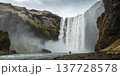 A colossal waterfall thunders down a sheer cliff face, creating mist and spray, with a person standing at the base enjoying the natural beauty A colossal waterfall thunders down a sheer cliff face, creating mist and spray, with a person standing at the base enjoying the natural beauty 137728578