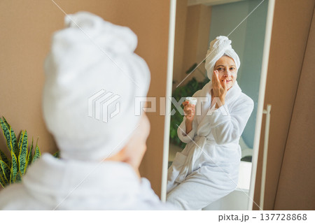 Mature adult old woman looking at mirror applying nourishing anti age face cream doing daily beauty routine. Senior woman with white mask creme on skin gets facial treatment Skin care aging skincare 137728868
