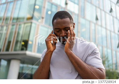 Sad tired lonely disappointed African man alone talking on smartphone on city street outdoor. Unhappy person making answering call by cellphone experiencing grief getting bad news. Stressed man Sad tired lonely disappointed African man alone talking on smartphone on city street outdoor. Unhappy person making answering call by cellphone experiencing grief getting bad news. Stressed man 137728914