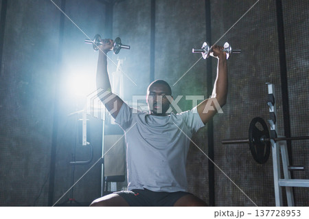 Fitness workout in gym. African American man bodybuilder picking up dumbbells in gym. Workout weight training biceps muscles with dumbbell in fitness club. Man doing sports exercise. Healthy lifestyle Fitness workout in gym. African American man bodybuilder picking up dumbbells in gym. Workout weight training biceps muscles with dumbbell in fitness club. Man doing sports exercise. Healthy lifestyle 137728953