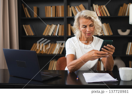 Confident stylish European middle aged senior woman using smartphone at workplace. Stylish older mature 60s lady businesswoman with cell phone in office. Boss leader using internet apps Confident stylish European middle aged senior woman using smartphone at workplace. Stylish older mature 60s lady businesswoman with cell phone in office. Boss leader using internet apps 137728981