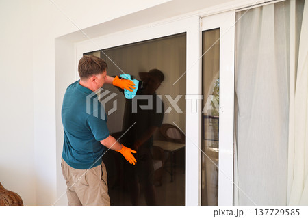 A man wipes dust from a large picture window in his home A man wipes dust from a large picture window in his home 137729585