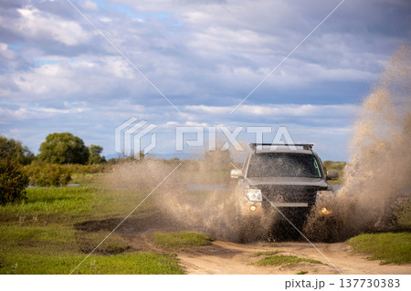 Japanese SUV moving by a puddle making a lot of water splashes Japanese SUV moving by a puddle making a lot of water splashes 137730383