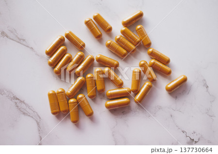 Premium flatlay with bright curcumin capsules scattered on white marble, contrasting vibrant turmeric hues with cool stone texture for a clean wellness aesthetic 137730664