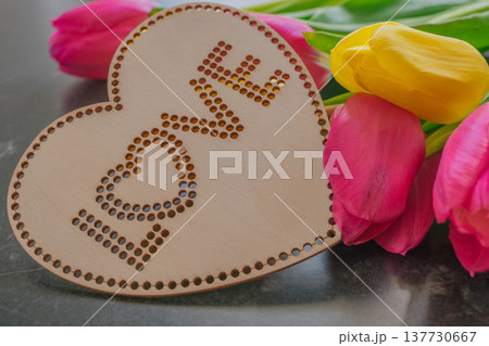 Dark moody composition of yellow and pink tulips on black marble with a wooden heart sign Love . High-contrast floral aesthetic for Mother's Day and spring branding 137730667
