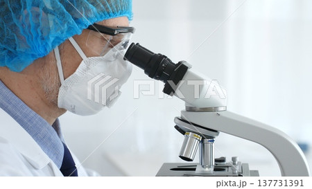 Male scientist wearing protective gear examining microscope slide, analyzing research sample in sterile laboratory environment. Health care and science concept Male scientist wearing protective gear examining microscope slide, analyzing research sample in sterile laboratory environment. Health care and science concept 137731391