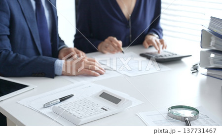 Calculator and magnifying glass over financial documents opposite financial team analyzing data, reviewing reports, collaborating at modern office workspace, close up view. Audit and taxes Calculator and magnifying glass over financial documents opposite financial team analyzing data, reviewing reports, collaborating at modern office workspace, close up view. Audit and taxes 137731467