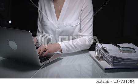 Businesswoman researching documents and accounting data with laptop and magnifying glass working late. Audit and taxes concept 137731594