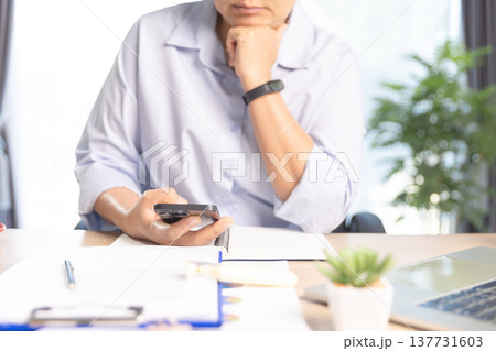 Business professional working on laptop at modern office desk with documents, smartphone and stationery, bright daylight by window. Concept of productivity, remote work and digital management. Business professional working on laptop at modern office desk with documents, smartphone and stationery, bright daylight by window. Concept of productivity, remote work and digital management. 137731603