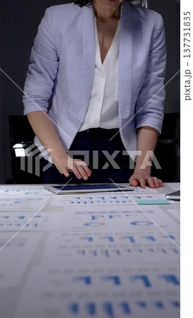 Businesswoman managing financial data, analyzing reports late at night, working overtime on a laptop, standing at a desk in a dark office, concentrating on strategic planning 137731835