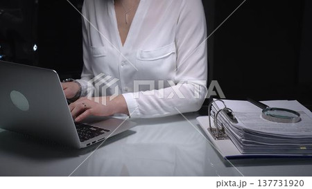Businesswoman researching documents and accounting data with laptop and magnifying glass working late. Audit and taxes concept 137731920
