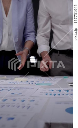 Business professionals analyzing marketing data graphs and financial charts on a desk at night, collaborating on a corporate project, discussing growth strategy Business professionals analyzing marketing data graphs and financial charts on a desk at night, collaborating on a corporate project, discussing growth strategy 137731943