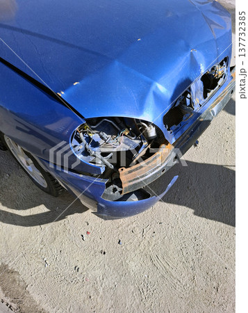 A wrecked car rests on the street with a damaged front end. The paint is chipped and rust is showing. The area looks deserted with no people around. A wrecked car rests on the street with a damaged front end. The paint is chipped and rust is showing. The area looks deserted with no people around. 137732385