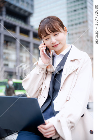外出先で通話をしながらノートパソコンを確認する若いビジネスウーマン 外出先で通話をしながらノートパソコンを確認する若いビジネスウーマン 137732680