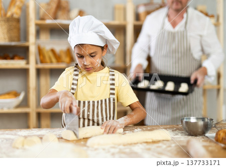 Little girl, baker assistant, cutting raw dough with knife 137733171