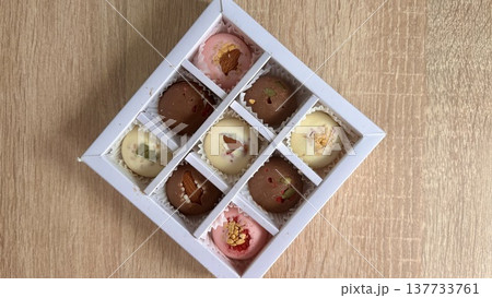 Delicious, sweet handmade chocolates made of white and milk chocolate with whole nuts in a gift box on a light background. High quality photo 137733761