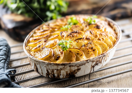 Golden-brown gratin potatoes, neatly arranged in a white ceramic bowl and garnished with fresh herbs. In Slovakia, however, this dish is known primarily at home as French potatoes 137734567