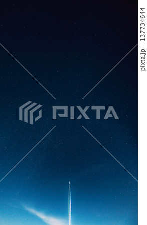 Airplane contrail cutting through a starry blue night sky with light clouds 137734644