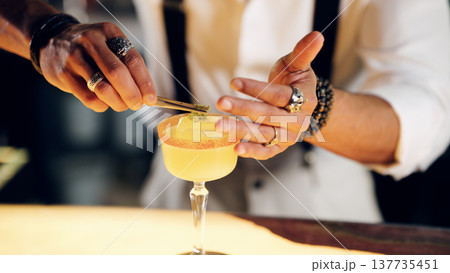 Bartender garnishing cocktail with tweezers at a bar 137735451